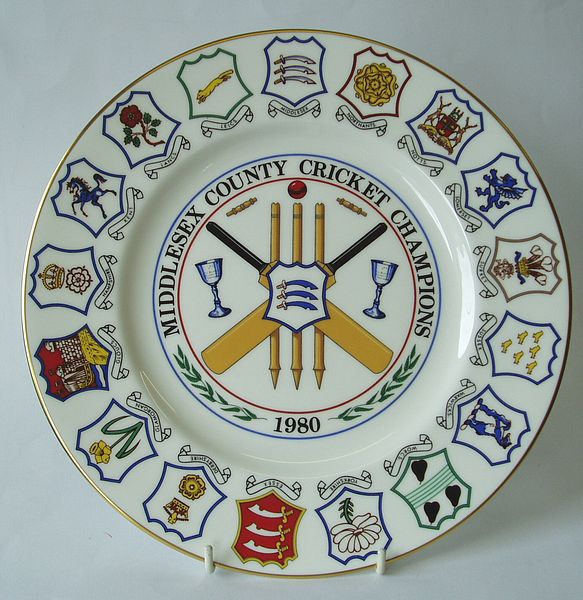 A Coalport china plate decorated with a central design of crossed bats and stumps and the county badge. The outer rim incorporates a design of seventeen county badges.