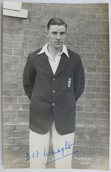 An original three-quarter length postcard photograph of Doug Wright, wearing his England blazer, with his arms behind his back.