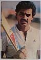 An original head and shoulders colour postcard photograph of Dilip Vengsarkar holding a bat.